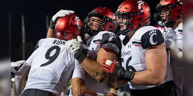 Cincinnati quarterback Desmond Ridder (9) is congratulated by offensive linemen Vincent McConnell, center, and Jake Renfro (56) after a touchdown run against SMU during the second half of an NCAA college football game Saturday, Oct. 24, 2020, in Dallas. (AP Photo/Jeffrey McWhorter)